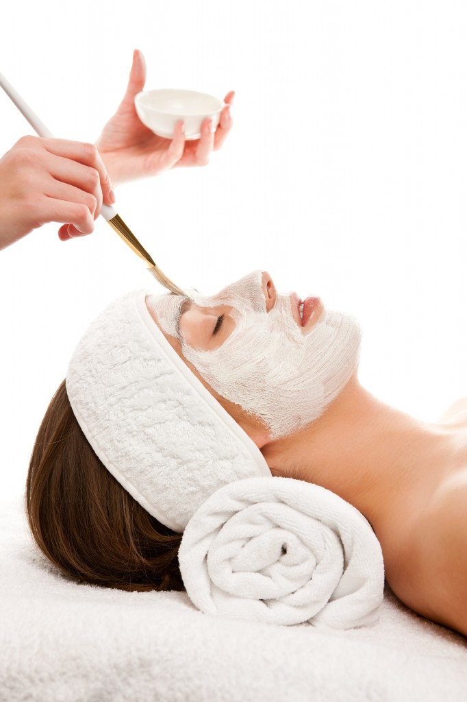 Woman receiving facial mask while lying on white towels